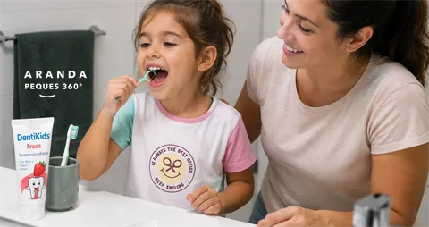 Madre ayudando a su hija a usar un arco dental infantil (flosser) frente al espejo del baño