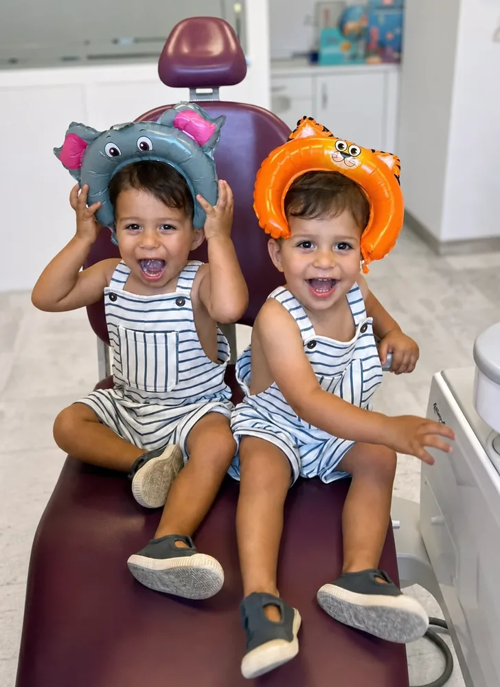 Dos niños sonriendo con gorros de animales en la consulta de odontopediatría de la Clínica Dental Aranda
